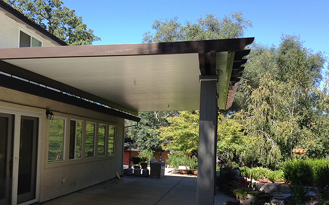 A rustic wooden pergola creates shade and extends the living space of a cozy home.